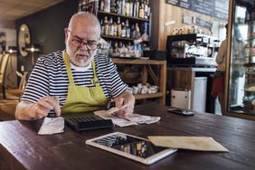 business owner sitting at table with calculator going over receipts