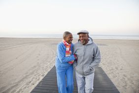 Senior couple walking arm in arm and laughing together on the beach.