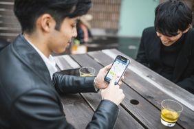 Young Japanese Man Using Smart Phone for Online Trading