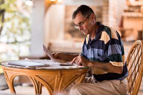 Senior man seriously evaluating paperwork at a small, round table at home