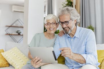 Mature couple sitting on couch use a digital tablet