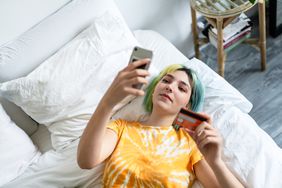  A woman in bed shops online with her phone and credit card.