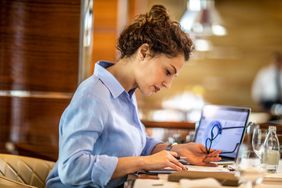 Businesswoman holding glasses looks at paper beside laptop