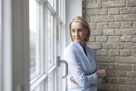 Mature woman looking sadly out a window.