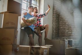 A couple takes a selfie in their new home, surrounded by moving boxes