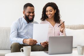  A young couple reviews a document while sitting on a couch in front of laptop