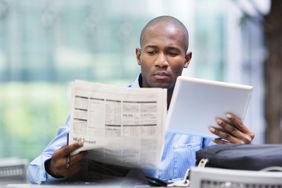 Young man checking the margin debt for stock investments in the newspaper and his his tablet