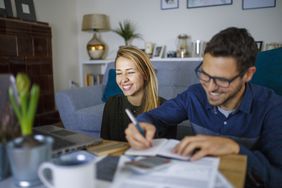 Laughing couple recording expenses in a notebook