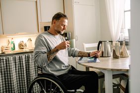 Man in wheelchair reading mail while holding coffee cup at home