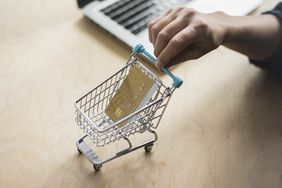 Hand pushing a mini shopping cart that holds a credit card across a desk