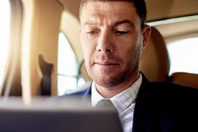 A businessman uses a tablet to check his investments while riding in a car