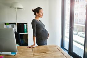 Pregnant woman standing in office looking out window