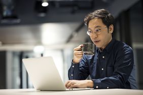 Bespectacled man with a coffee mug working on his laptop