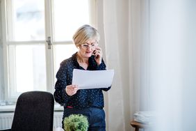 Mature woman looking at paperwork talks on cellphone