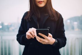 Young Woman With Face Obscured Holding Cell Phone and Using It Outside.
