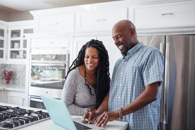 A smiling couple working at a laptop on their kitchen counter