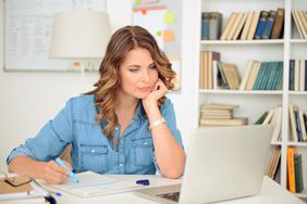 Woman seated in front of computer in her home office, writing notes