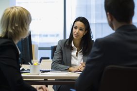 Female business executive speaks sitting at desk speaks to two colleagues