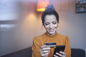 Smiling woman using smartphone and credit card at home