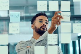 A man looks at sticky notes on a glass wall. 
