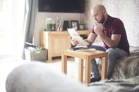Man reading latest interest statement with cup of coffee in his living room