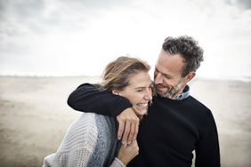 An older couple hug each other and smile on the beach.