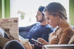 couple with newspaper and cell phone in coffee shop