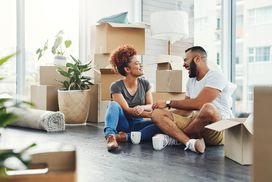 Young couple on floor of living room, taking a break from unpacking boxes in new home