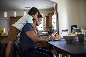 Man working on laptop at home while child watches