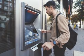 man with suitcase depositing cash into an ATM 