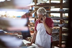 Female business owner on phone in workshop while looking at laptop