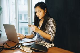 Woman holding credit card while shopping online on laptop while sitting at home