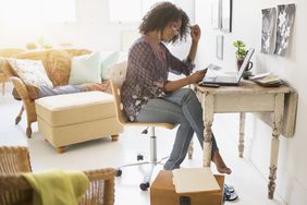 Woman sits at desk in home looking at application in front of a laptop