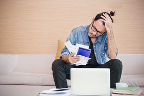 A worried man holds his head in his hand while staring at a laptop and a pile of bills, deciding whether to file a CFPB complaint