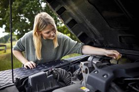 Young woman checking car with open hood