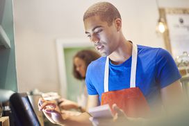 Young man wearing apron uses touch-screen computer to place order