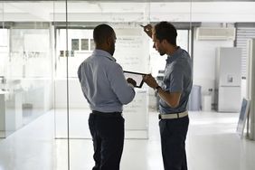 Businessmen holding digital tablet and writing strategy on glass wall