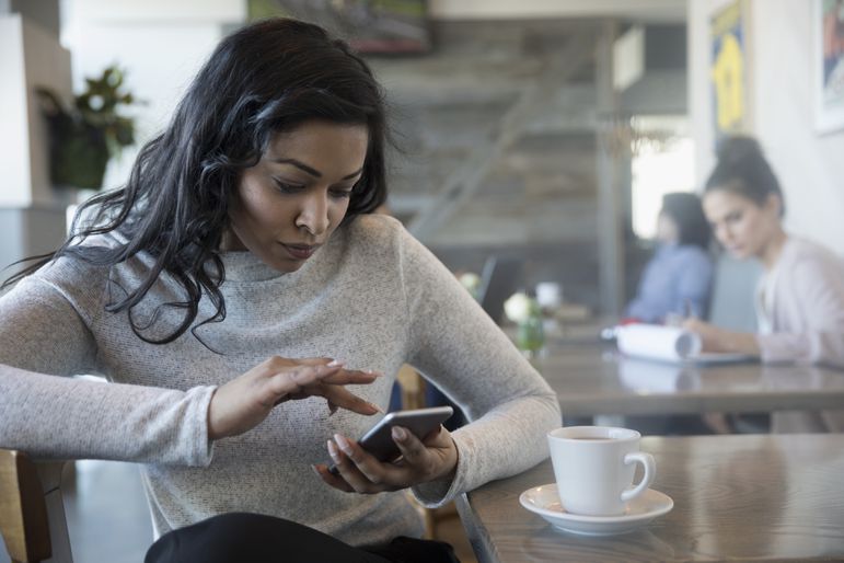 Woman using smart phone, drinking coffee in cafe