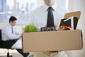 Fired employee walking out of office with a box filled with supplies.