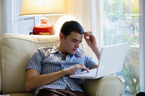 Young person researching investment options in living room on laptop