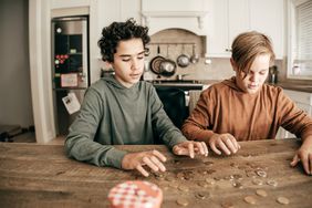 Two kids count coins laid out on a kitchen counter