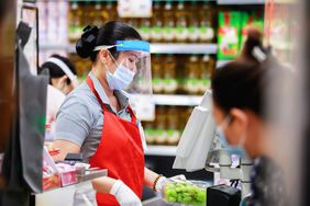 Supermarket cashier in medical protective mask working at checkout 