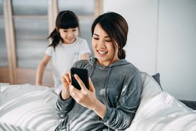 Smiling woman uses smartphone as young daughter watches