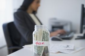 Jar labeled 401k filled with money and a woman working in the background