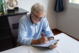 Gray-Haired Man in Blue Shirt Reviewing Application Form at Home Dining Table.