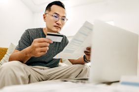 Person with glasses looking at credit card bill while holding a card. 