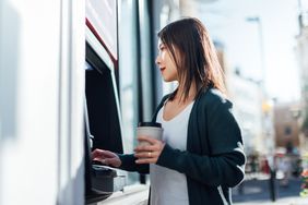 Woman at ATM holds her bank card and coffee cup