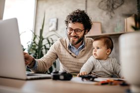 Smiling father and infant son sit at a desk looking at something on computer screen