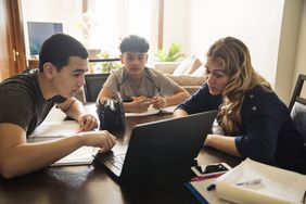 Woman showing teenage boys information on computer at home