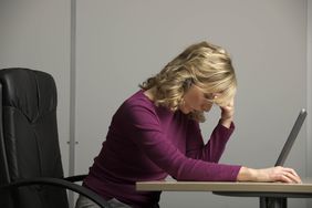 Woman at desk, head bowed over computer, as she grapples alone with illegal retaliation in her workplace